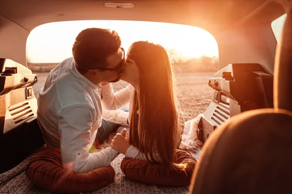 Beyaz gömlekli ve kot pantolonlu genç mutlu çift yeni arabalarında yolculuğun tadını çıkarıyor, Sahada güzel bir gün batımı, tatil ve seyahat konsepti — Stok fotoğraf