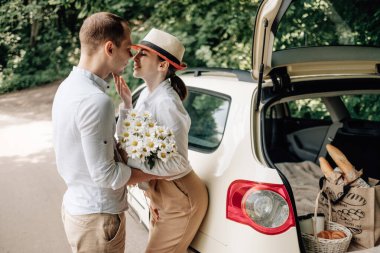 Beyaz tişörtlü genç mutlu çift arabanın yanında eğleniyor, hafta sonu şehir dışında, tatiller ve yolculuk konsepti.