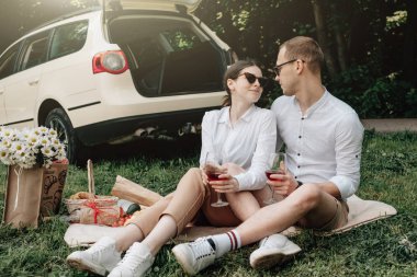 Beyaz tişörtlü genç mutlu çift arabanın yanında eğleniyor, hafta sonu şehir dışında, tatiller ve yolculuk konsepti.