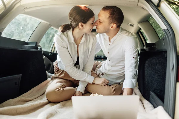Fiatal boldog pár öltözött Alike fehér póló Ül az autóban csomagtartó laptoppal és popcorn az úton, hétvégén városon kívül, Ünnepek és Road Trip Concept — Stock Fotó