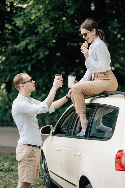 Joven pareja feliz vestida como en camiseta blanca divirtiéndose cerca del coche, fin de semana fuera de la ciudad, días festivos y concepto de viaje por carretera — Foto de Stock