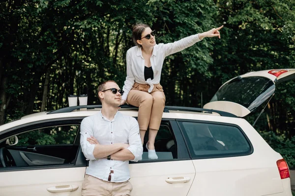 Joven pareja feliz vestida como en camiseta blanca divirtiéndose cerca del coche, fin de semana fuera de la ciudad, días festivos y concepto de viaje por carretera — Foto de Stock