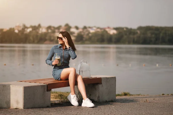 Una hermosa chica morena vestida con pantalones vaqueros bebidas cóctel — Foto de Stock