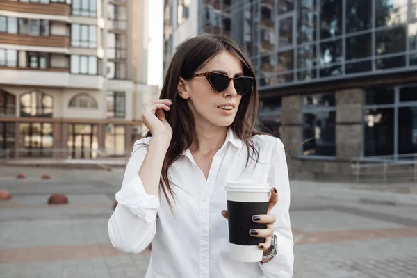 Retrato de una chica de moda vestida con jeans y camisa blanca bebiendo café y usando su teléfono inteligente, dama de negocios, concepto de poder de la mujer —  Fotos de Stock