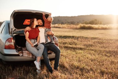 Mutlu Genç Aile Anne ve Baba ve Küçük Oğulları Hafta Sonu Keyifli Pikniği Güneşli Gün batımı, Tatil ve Yolculuk Konsepti 'nde, Şehir dışındaki Araba Sandığında Oturuyorlar.