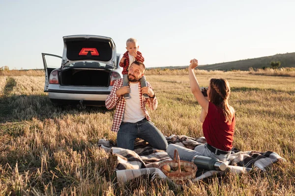 Mutlu Genç Aile Anne ve Baba ve Küçük Oğulları Hafta Sonu Keyifli Pikniği. Ekoseli Ekoseli Arabanın Üzerinde, Şehrin Dışında, Sunny Day Sunset, Tatil ve Yolculuk Konsepti 'nde.
