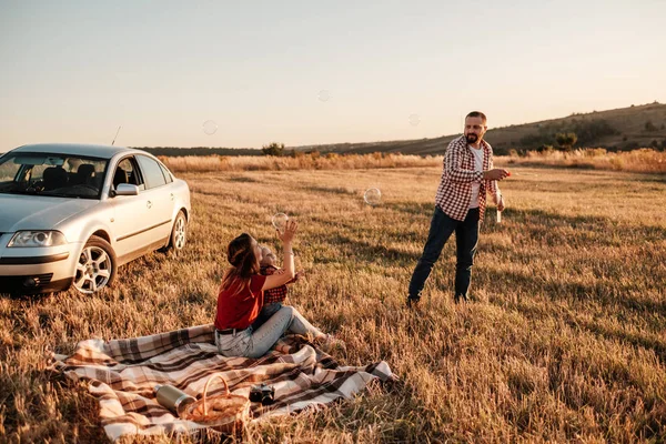 Glad ung familj mamma och pappa med sin lilla son Njuter av sommar helg picknick på bilen utanför staden, leka med bubblor — Stockfoto