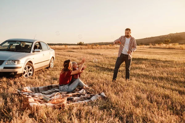 Glad ung familj mamma och pappa med sin lilla son Njuter av sommar helg picknick på bilen utanför staden, leka med bubblor — Stockfoto