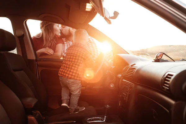 Happy Young Family Maman et papa avec leur fils Petit conducteur profitant week-end d'été pique-nique sur la voiture à l'extérieur de la ville sur le terrain au coucher du soleil, vacances et voyage Concept — Photo