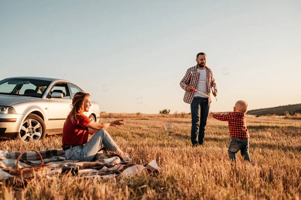 Happy Young Family Mom and Dad with Their Little Son Enjoying Summer Weekend Picnic on the Car Outside the City, Play with Bubbles — Stok Foto