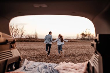 Beyaz Gömlekli ve Kot Giyen Genç Mutlu Çift Yeni Araba Bagajlarında Oturuyor, Sahada Güzel Günbatımı, Tatil ve Seyahat Konsepti