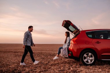 Beyaz Gömlekli ve Kot Giyen Genç Mutlu Çift Yeni Araba Bagajlarında Oturuyor, Sahada Güzel Günbatımı, Tatil ve Seyahat Konsepti