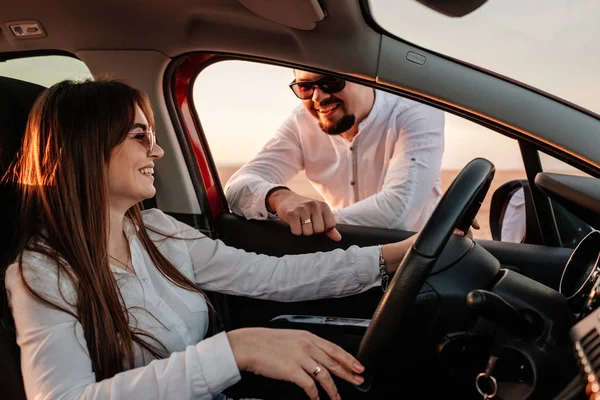 Young Happy Couple Dressed Alike in White Shirt and Jeans Enjoying Road Trip at Their New Car, Beautiful Sunset on the Field, Vacation and Travel Concept — 스톡 사진