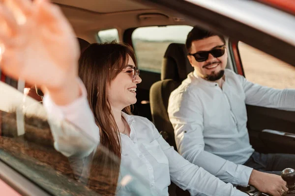 Young Happy Couple Dressed Alike in White Shirt and Jeans Enjoying Road Trip at Their New Car, Beautiful Sunset on the Field, Vacation and Travel Concept — 스톡 사진