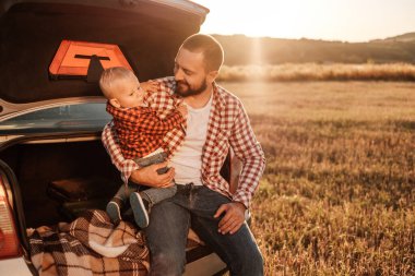 Küçük oğluyla mutlu bir baba. Yaz haftasının tadını çıkarıyor. Güneşli gün batımında şehrin dışındaki kırda.