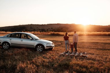 Mutlu Genç Aile Anne ve Baba ve Küçük Oğulları Hafta Sonu Keyifli Pikniği Arabayla Şehrin dışında Sunny Day Sunset, Tatil ve Yolculuk Konsepti 'nde