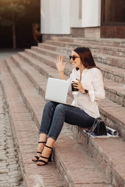 Retrato de uma menina elegante vestida em jeans e camisa branca segurando laptop e café quente, trabalhador freelance, senhora de negócios, conceito de poder da mulher — Fotografia de Stock