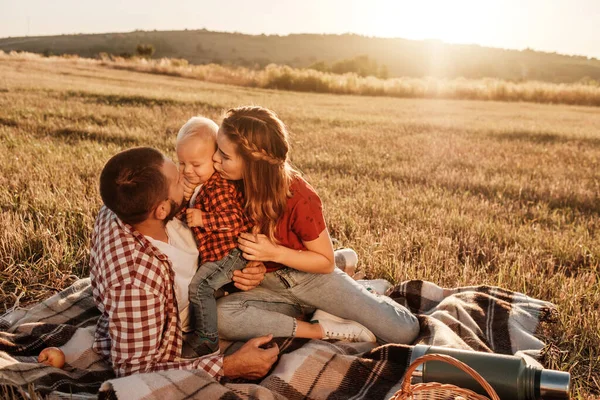 Счастливая молодая семья мама и папа со своим маленьким сыном Наслаждаясь летние выходные пикник за городом в поле в солнечный день заката, Концепция времени отпуска — стоковое фото