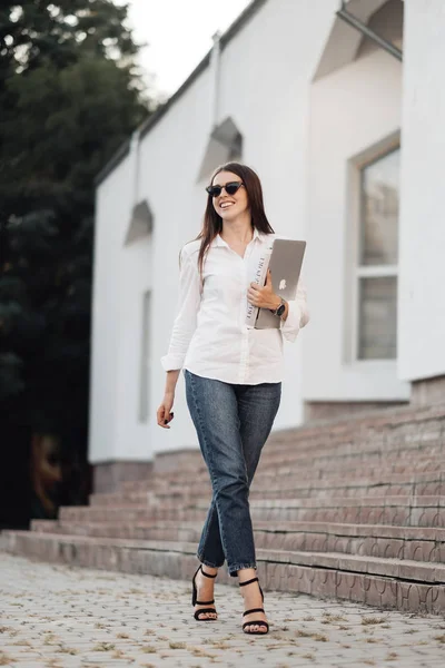 Tarnopol, Ukraina - 28 sierpnia 2019: Portret jednej modnej dziewczyny ubranej w dżinsy i białą koszulę z Apple Laptop Macbook Air, wolny strzelec, Business Lady, kobieta Power Concept — Zdjęcie stockowe