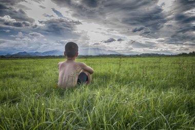 Yeşil çimenlerin üzerinde oturan küçük çocuk