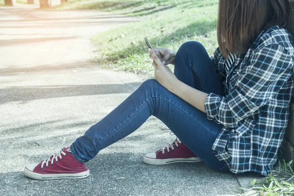 Egy fiatal nő ül a parkban, használ neki telefont — Stock Fotó