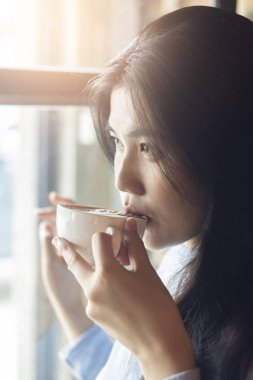 Asyalı kadın sıcak kahve içiyor. 