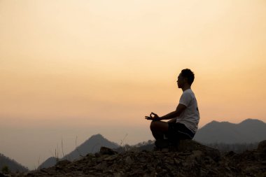 Siluet Asyalı adam yogası günbatımında.