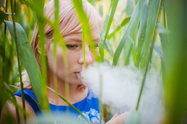 portrait nude vaping girl in sedge. young blonde woman standing in the reeds and smoking an electronic cigarette, blowing the smoke vapor