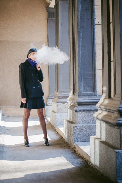 Retrato de mulher bonita nova com cabelo branco, em um casaco preto, uma saia e um chapéu preto, fumando um cigarro eletrônico — Fotografia de Stock