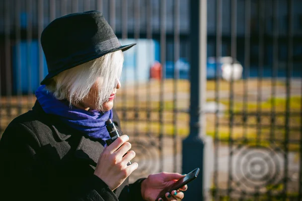 Ritratto di giovane bella donna con i capelli bianchi, in un cappotto nero, una gonna e un cappello nero, parlando al cellulare per strada. comunicazione telefonica, collegamento, piacevole conversazione sul business — Foto Stock