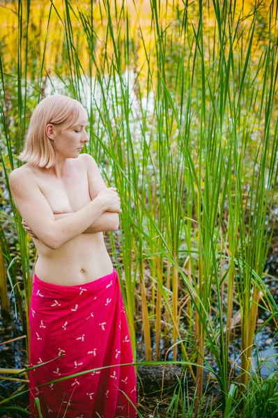 Nude κορίτσι στην σπαθόχορτο. νεαρή ξανθιά γυναίκα με τα γυμνά στήθη, τυλιγμένο σε ένα κόκκινο πανί, στέκεται στα καλάμια — Φωτογραφία Αρχείου