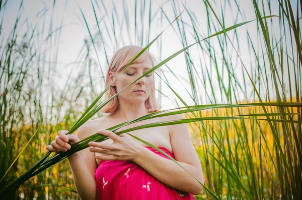 Naakt meisje in zegge. jonge blonde vrouw met blote borsten, verpakt in een rode doek, permanent in het riet — Stockfoto