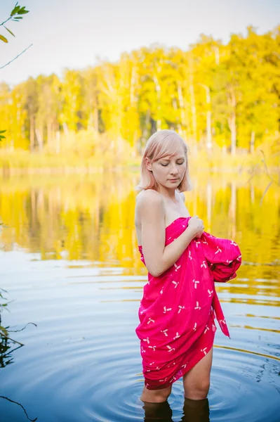 Оголена дівчина в спокусі. молода блондинка з голими грудьми, загорнута в червону тканину, стоїть в очереті — стокове фото
