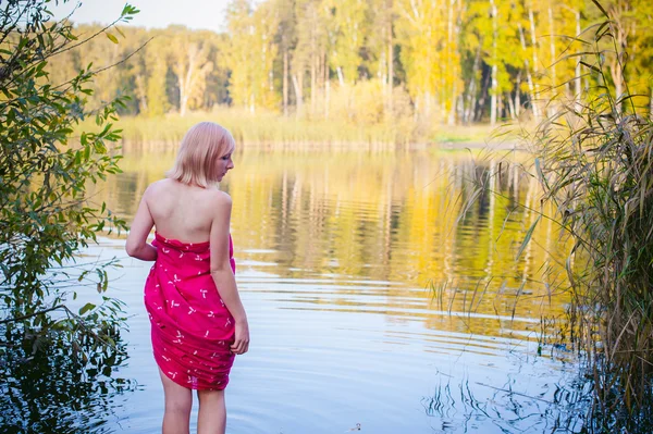 Fille nue à carex. jeune femme blonde aux seins nus, enveloppée dans un tissu rouge, debout dans les roseaux — Photo