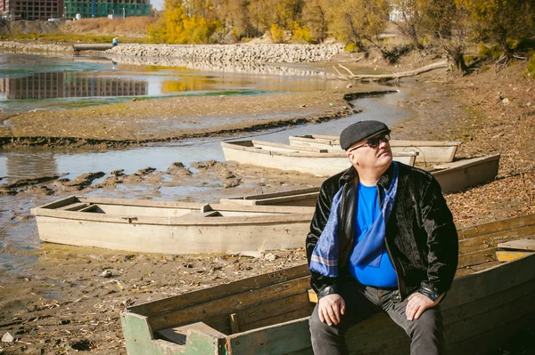 Hombre adulto sentado en un viejo barco de madera y mira a la distancia — Foto de Stock