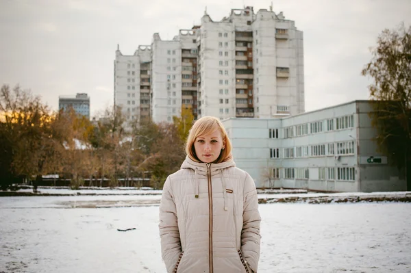 Blonde girl in the yard of a house. the first snow in the city — Stock Photo, Image