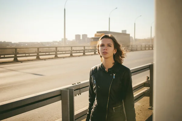 girl goes on road bridge. lonely young woman in black Leather jacket autumn, walking over the bridge which goes transport.