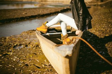 Mavi kot pantolon ve kahverengi botları kızın bacakları ince. kalkık teknede shore, sarı sonbahar yaprakları kız oturdu