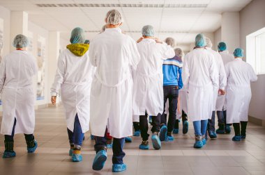 Grup endüstriyel üretimde insan. insanlar Beyaz önlük kamerada geri dön ve galoş fabrika turnede var