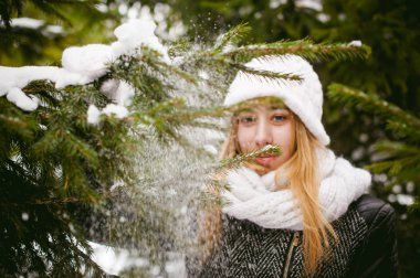 Sevimli kadın kar açık havada arka plan üzerinde beyaz atkı ve şapka örme ceket ve bulanık köknar kış dallarında portre
