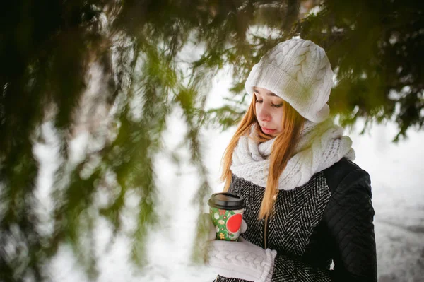 Portrait of cute woman in white scarf and hat knitted coat on outdoors background of snow and blurred fir branches in winter. — Stock Photo, Image