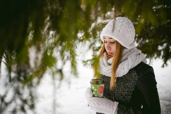 Portré, aranyos nő, és fehér kendő kalap kötött kabát a szabadban háttér a hó, és homályos fenyő ágak, télen. — Stock Fotó