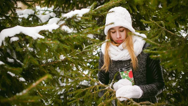 雪の屋外背景に白いスカーフと帽子ニットのコートのかわいい女性と冬のぼやけのモミの枝の肖像画. — ストック写真