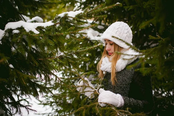 Πορτρέτο του χαριτωμένο γυναίκα στο λευκό κασκόλ και καπέλο πλεκτό παλτό σε εξωτερικούς χώρους φόντο του χιονιού και θολή κλαδιά έλατου το χειμώνα. — Φωτογραφία Αρχείου