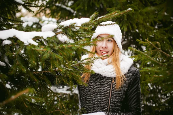 Porträtt av söt kvinna i vit halsduk och mössa stickad kappa på utomhus bakgrund av snö och suddig fir grenar på vintern. — Stockfoto