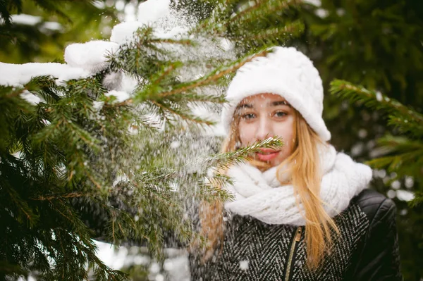 Porträtt av söt kvinna i vit halsduk och mössa stickad kappa på utomhus bakgrund av snö och suddig fir grenar på vintern — Stockfoto