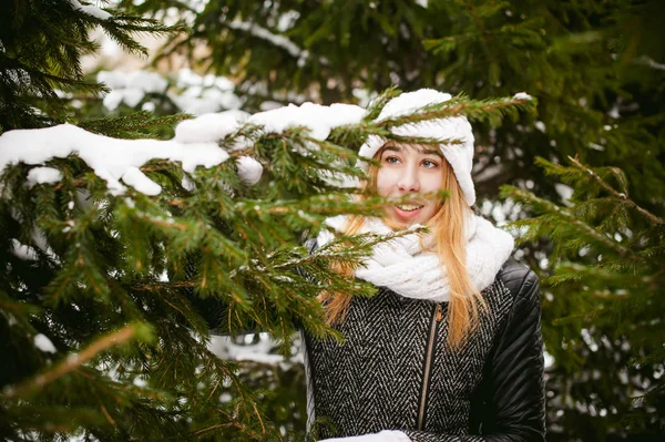 Porträtt av söt kvinna i vit halsduk och mössa stickad kappa på utomhus bakgrund av snö och suddig fir grenar på vintern — Stockfoto