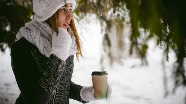 Ritratto di donna carina in sciarpa bianca e cappello cappotto lavorato a maglia su sfondo esterno di neve e rami di abete sfocati in inverno — Foto Stock