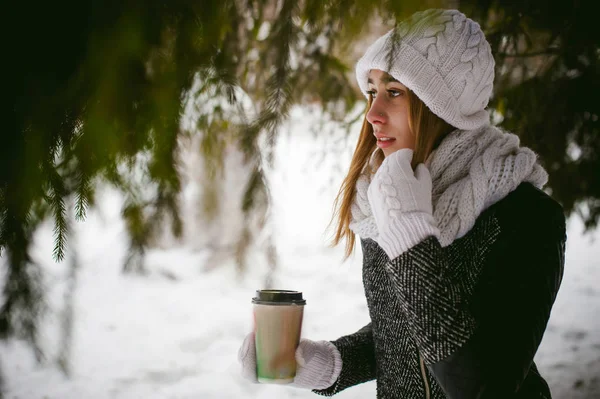Portrait de jolie femme en écharpe blanche et chapeau manteau tricoté sur fond extérieur de neige et branches de sapin floues en hiver . — Photo