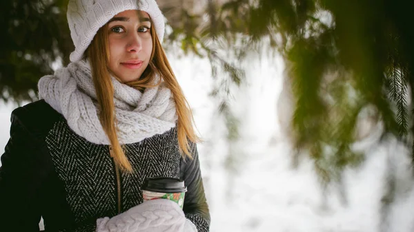 Ritratto di donna carina in sciarpa bianca e cappello cappotto lavorato a maglia su sfondo esterno di neve e rami di abete sfocati in inverno . — Foto Stock